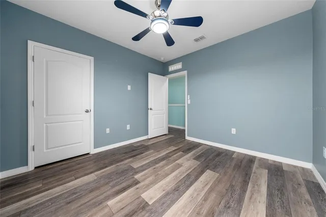 an empty room with wooden floor ceiling fan and windows