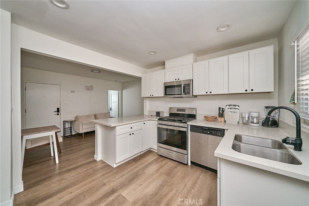 8734 Ramsgate Avenue Los Angeles, CA 90045 - Photo 7 of 19 a kitchen with granite countertop a stove top oven a sink dishwasher and white cabinets with wooden floor