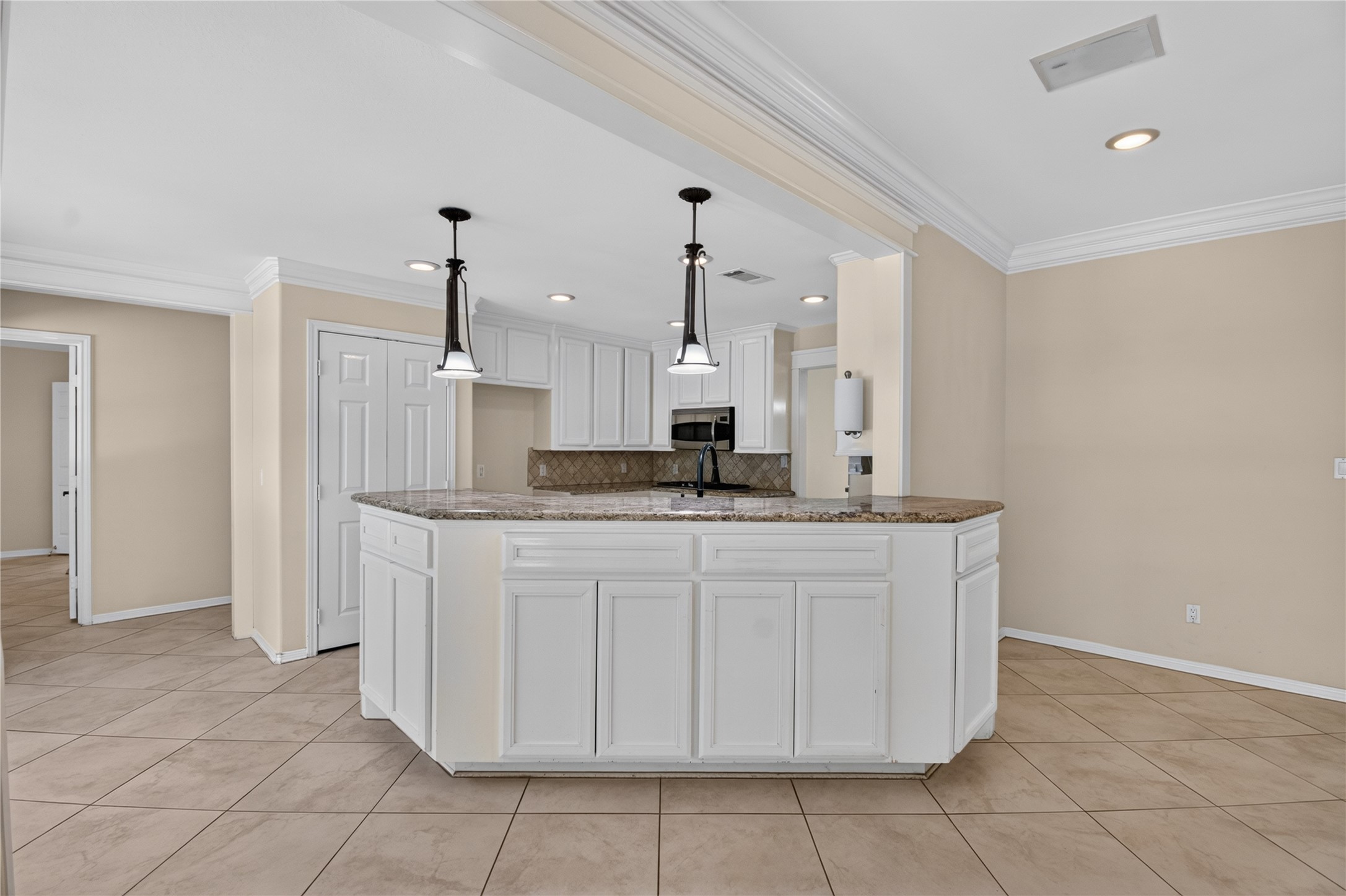 20203 Timber Ridge Drive Magnolia, TX 77355 - Photo 12 of 49 The countertops feature a warm, speckled granite. White raised-panel cabinets offer lenty of storage and creating a clean, timeless look. A matte black, high-arc pull-down faucet is installed at the island sink, providing a contemporary touch. Large beige ceramic floor tiles run throughout the space, enhancing durability and creating a seamless flow into the adjacent living area.