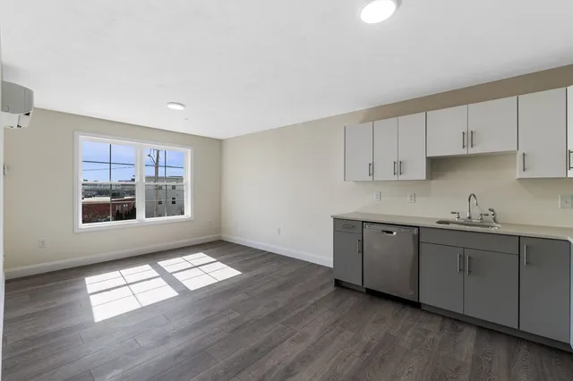 a kitchen with granite countertop a stove a sink and white cabinets with wooden floor
