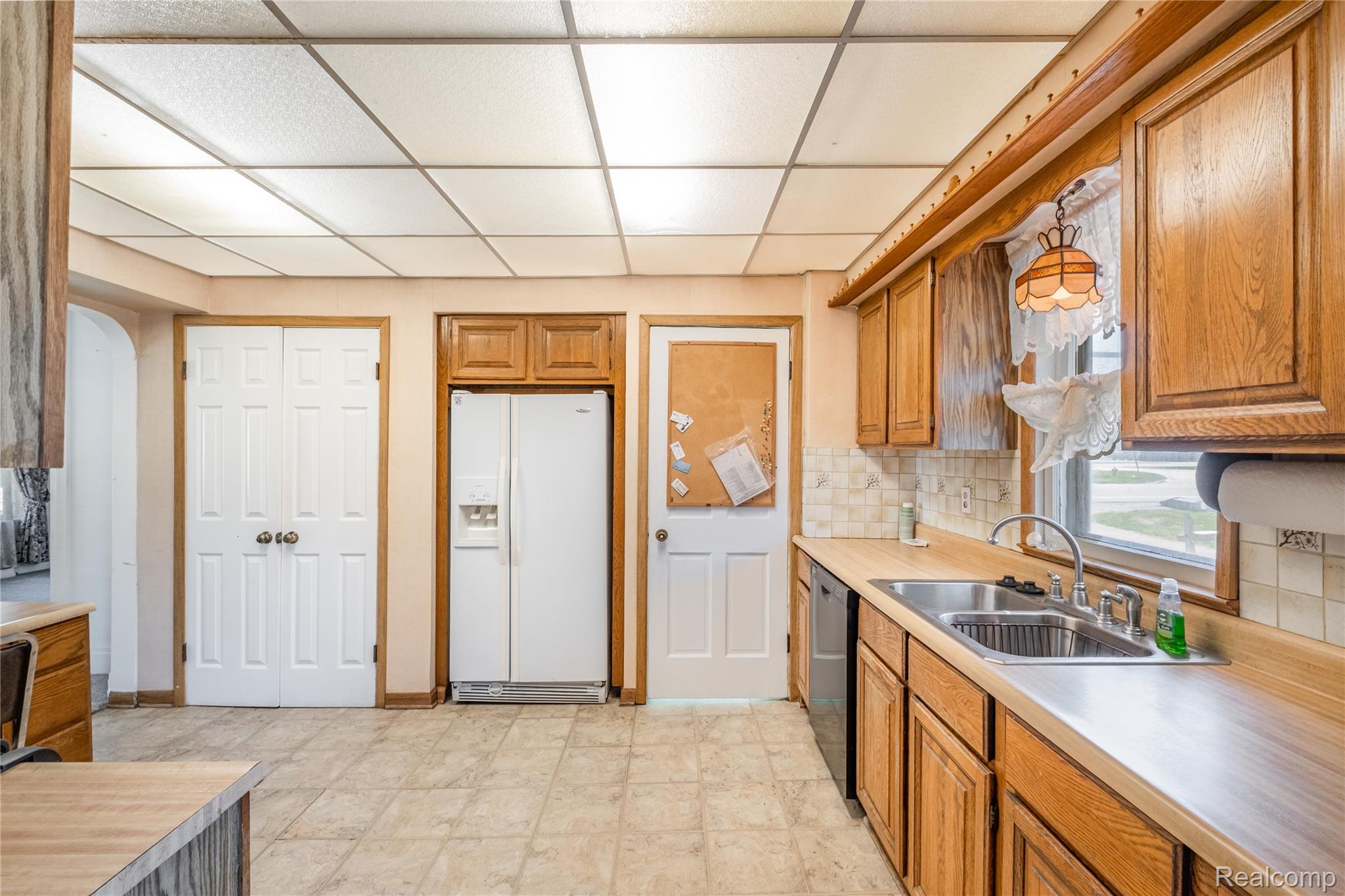 5447 North State Road Davison, MI 48423 - Photo 7 of 29 Kitchen featuring brown cabinetry, white refrigerator with ice dispenser, decorative backsplash, a paneled ceiling, and light countertops