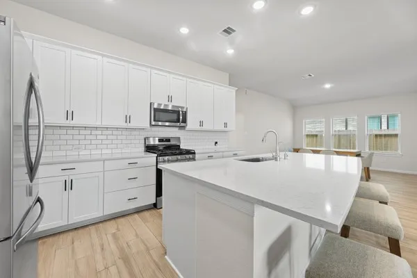 a kitchen with stainless steel appliances granite countertop a sink a stove a refrigerator and white cabinets