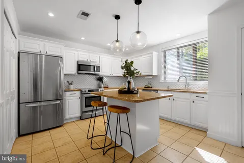 a kitchen with stainless steel appliances granite countertop a refrigerator a sink dishwasher a stove and white cabinets with wooden floor