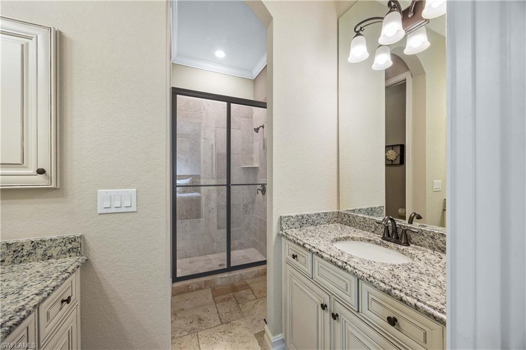 9852 Corso Bello Drive Naples, FL 34113 - Photo 37 of 50 Full bathroom with vanity, stone tile flooring, a textured wall, crown molding, and a stall shower