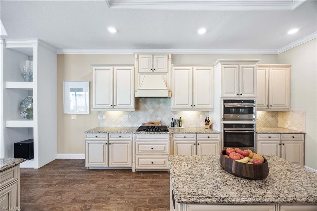 9852 Corso Bello Drive Naples, FL 34113 - Photo 3 of 50 Kitchen featuring light stone countertops, dark wood-type flooring, double oven, crown molding, and premium range hood