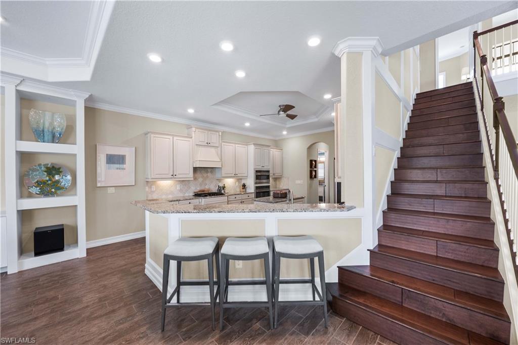 9852 Corso Bello Drive Naples, FL 34113 - Photo 5 of 50 Kitchen with a kitchen breakfast bar, light stone countertops, built in features, wood finish floors, and arched walkways