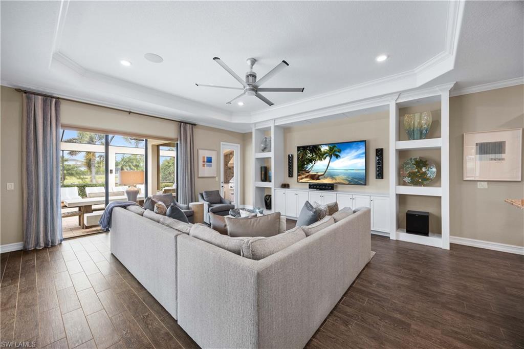 9852 Corso Bello Drive Naples, FL 34113 - Photo 8 of 50 Living area with a ceiling fan, dark wood-style floors, built in features, a tray ceiling, and ornamental molding