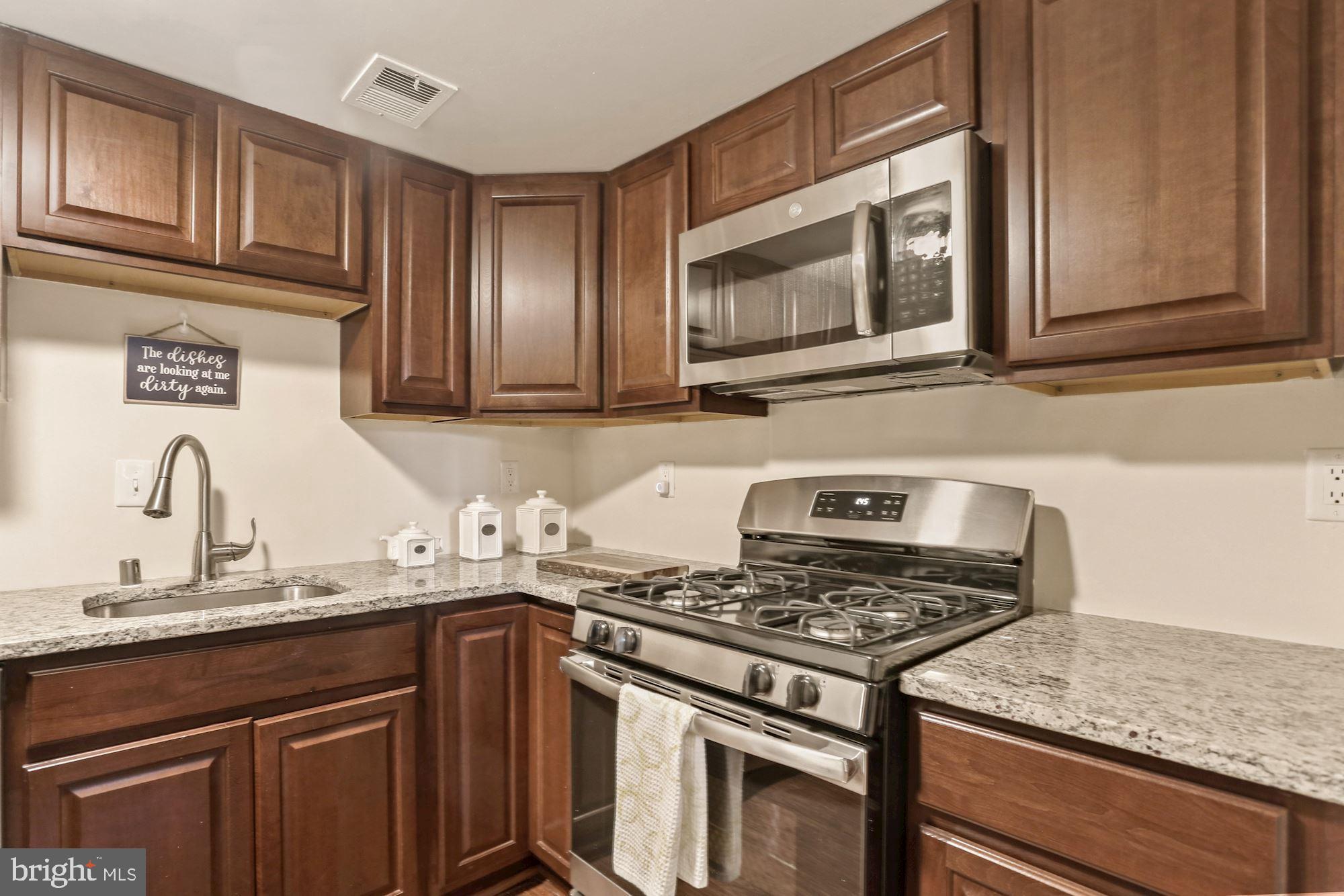a kitchen with granite countertop a stove top oven cabinetry a sink and a microwave