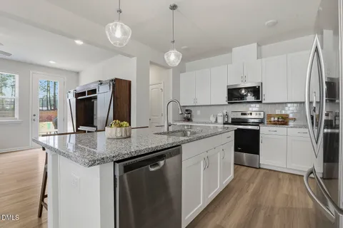 a kitchen with stainless steel appliances a dining table chairs refrigerator and microwave