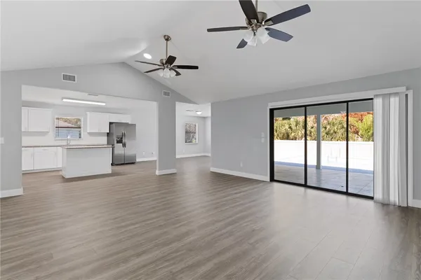 an empty room with wooden floor a ceiling fan and windows