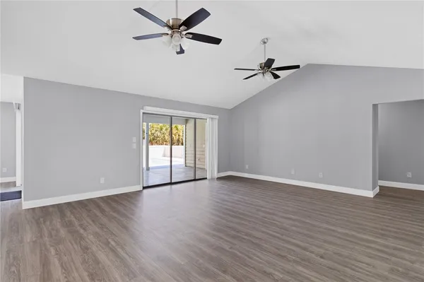 an empty room with wooden floor ceiling fan and windows