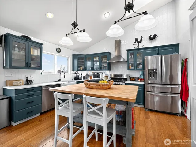 a kitchen with stainless steel appliances kitchen island granite countertop a refrigerator a stove a sink a dining table and chairs with wooden floor