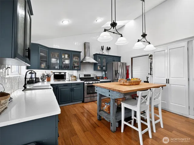 a kitchen with stainless steel appliances granite countertop a stove a refrigerator a kitchen island a dining table and chairs with wooden floor