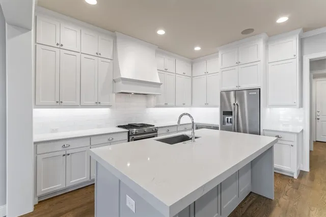 a kitchen with stainless steel appliances a sink a stove a refrigerator and white cabinets