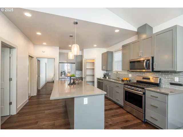 a kitchen with stainless steel appliances granite countertop a refrigerator a stove top oven a sink dishwasher and white cabinets with wooden floor