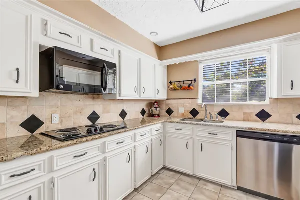 a kitchen with stainless steel appliances granite countertop white cabinets sink and window