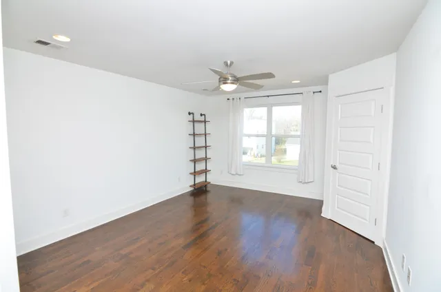 an empty room with wooden floor chandelier fan and windows
