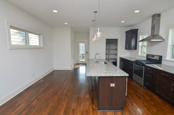 a kitchen with stainless steel appliances granite countertop wooden cabinets a stove a sink and a wooden floor