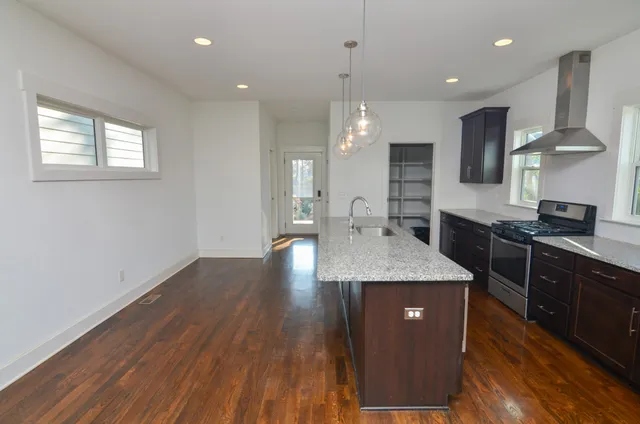 a kitchen with stainless steel appliances granite countertop wooden cabinets a stove a sink and a wooden floor