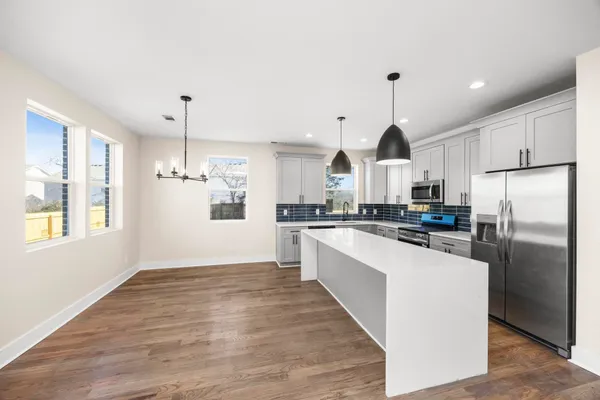 a kitchen with stainless steel appliances granite countertop a refrigerator a sink dishwasher a stove and white cabinets with wooden floor