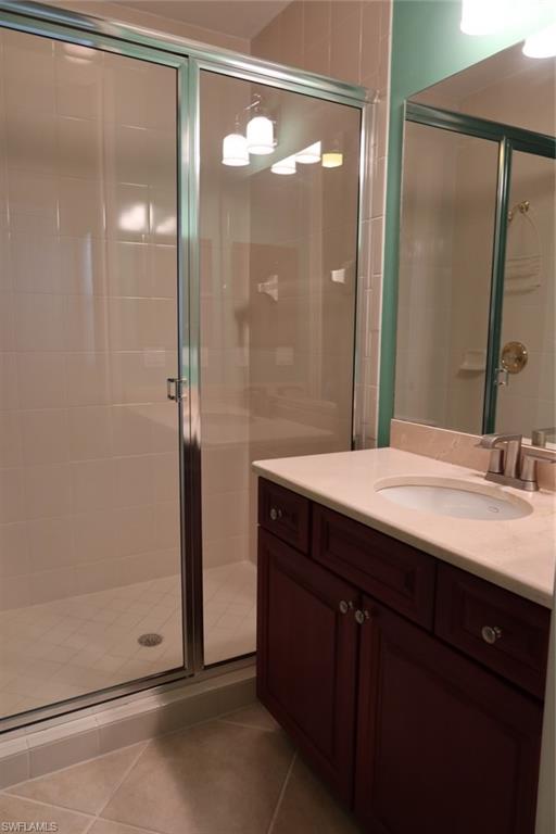 7168 Lemuria Circle, Unit 1701 Naples, FL 34109 - Photo 29 of 39 Bathroom featuring a glass-enclosed shower with tile surround, a dark wood-finish vanity with an integrated sink, a light-toned countertop, and brushed nickel fixtures