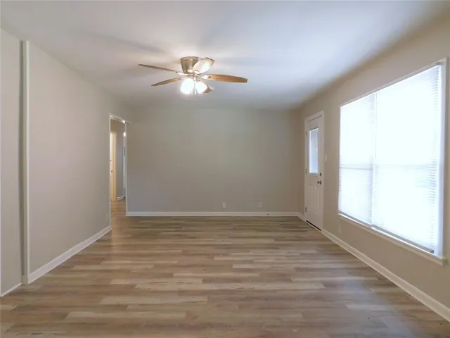 an empty room with wooden floor fan and windows