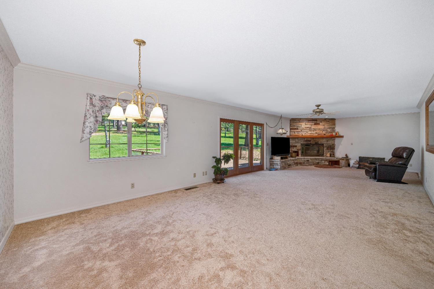 5215 Faraway Road Greenwood, CA 95635 - Photo 14 of 46 unfurnished living room with ceiling fan, carpet, hanging lights, ornamental molding, and a stone fireplace