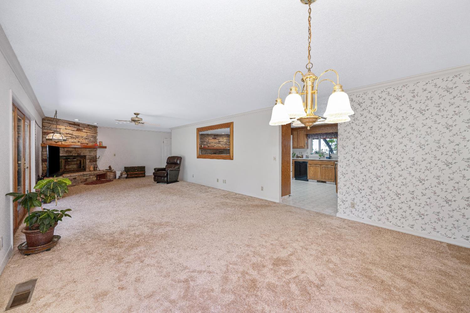5215 Faraway Road Greenwood, CA 95635 - Photo 17 of 46 unfurnished living room with ornamental molding, a stone fireplace, light carpet, a chandelier, and ceiling fan