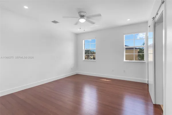 a view of an empty room with wooden floor and a ceiling fan