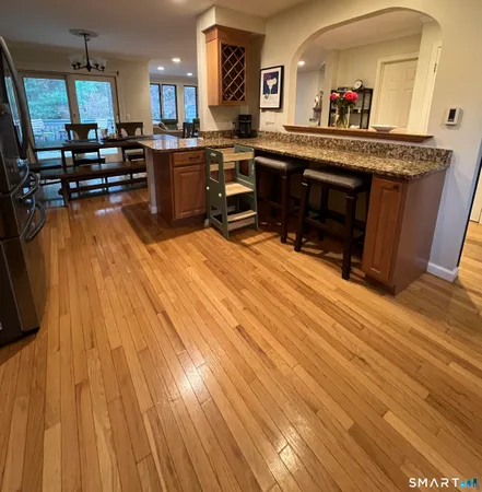 a living room with stainless steel appliances kitchen island granite countertop a sink dishwasher a stove and a dining table with wooden floor