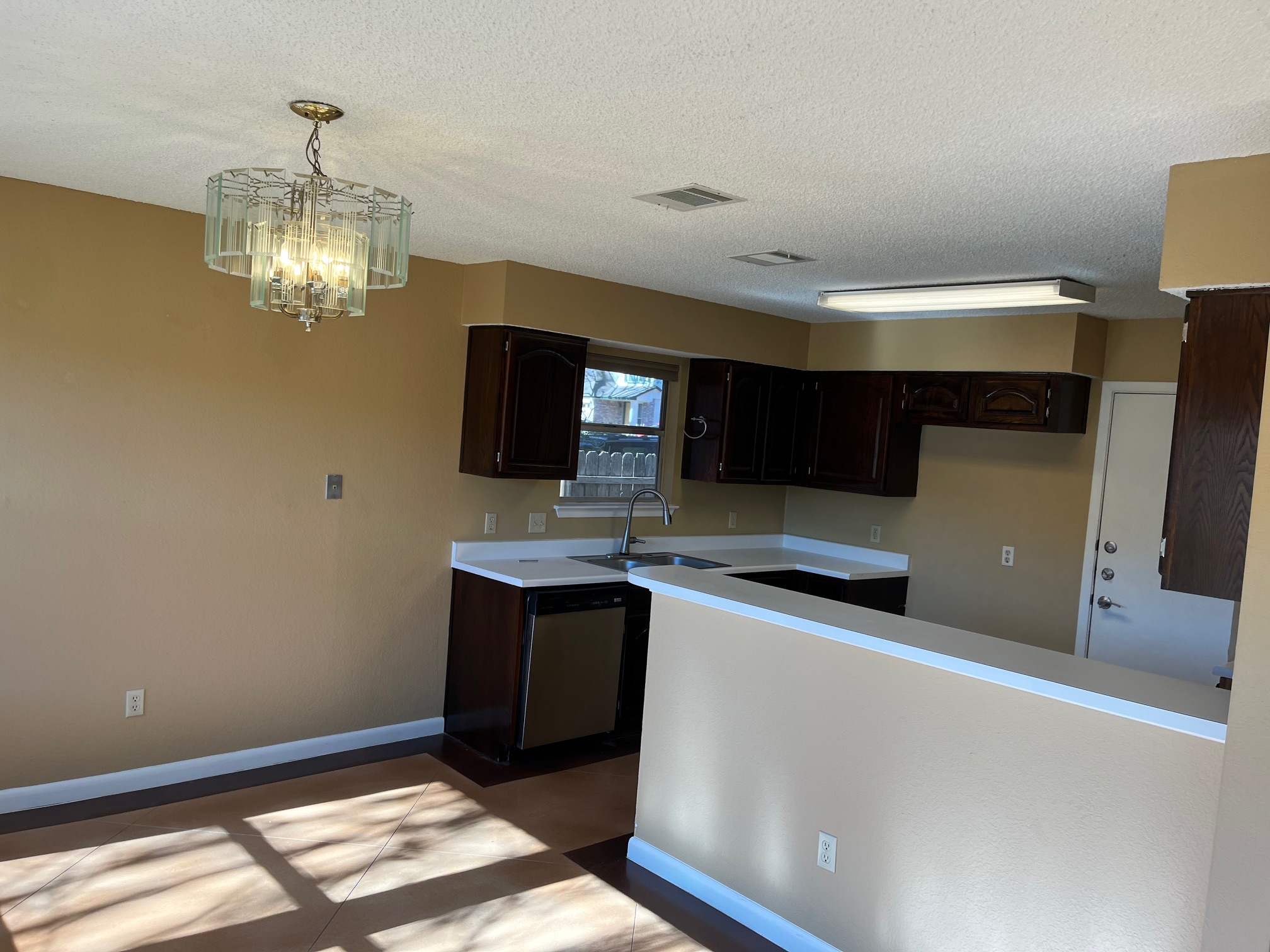 12919 Marimba Trail Austin, TX 78729 - Photo 11 of 20 Kitchen with light countertops, dark wood finish cabinetry, a textured ceiling, a chandelier, and stainless steel dishwasher