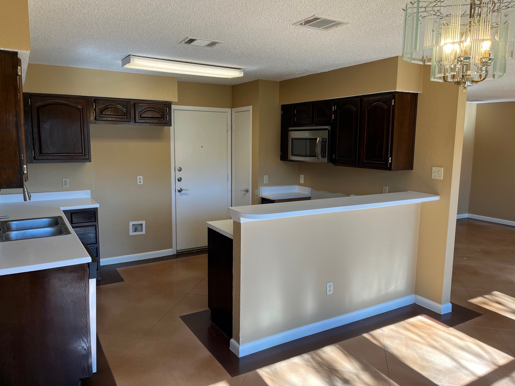 12919 Marimba Trail Austin, TX 78729 - Photo 10 of 20 Kitchen featuring light countertops, stainless steel microwave, a textured ceiling, dark wood finish cabinets, and a chandelier