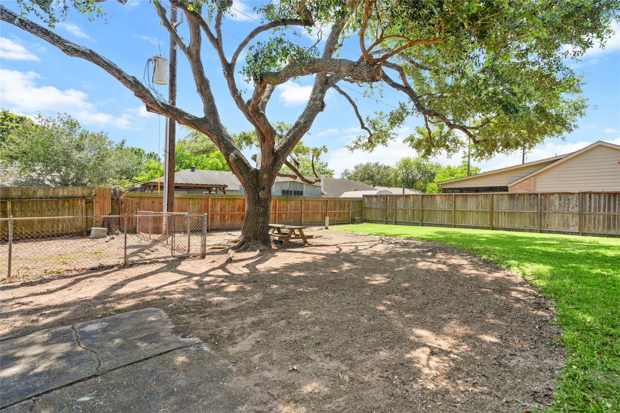 6610 Blue Ridge Drive Richmond, TX 77469 - Photo 23 of 24 This photo showcases a spacious backyard with lush green grass, a large mature tree providing shade, and a wooden fence for privacy. The side of the house features brick siding and sliding glass doors, offering easy access to outdoor living.