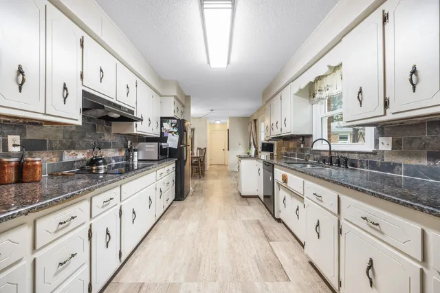a large kitchen with granite countertop lots of white cabinets and stainless steel appliances