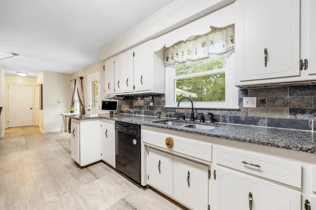 a kitchen with granite countertop white cabinets white appliances a sink and a window