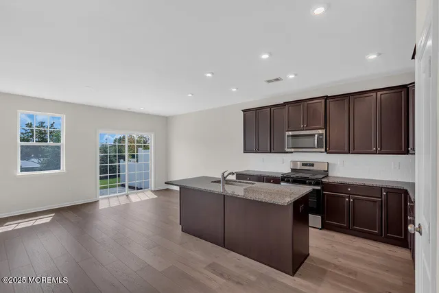 a kitchen with stainless steel appliances granite countertop wooden cabinets a stove a sink and a wooden floor