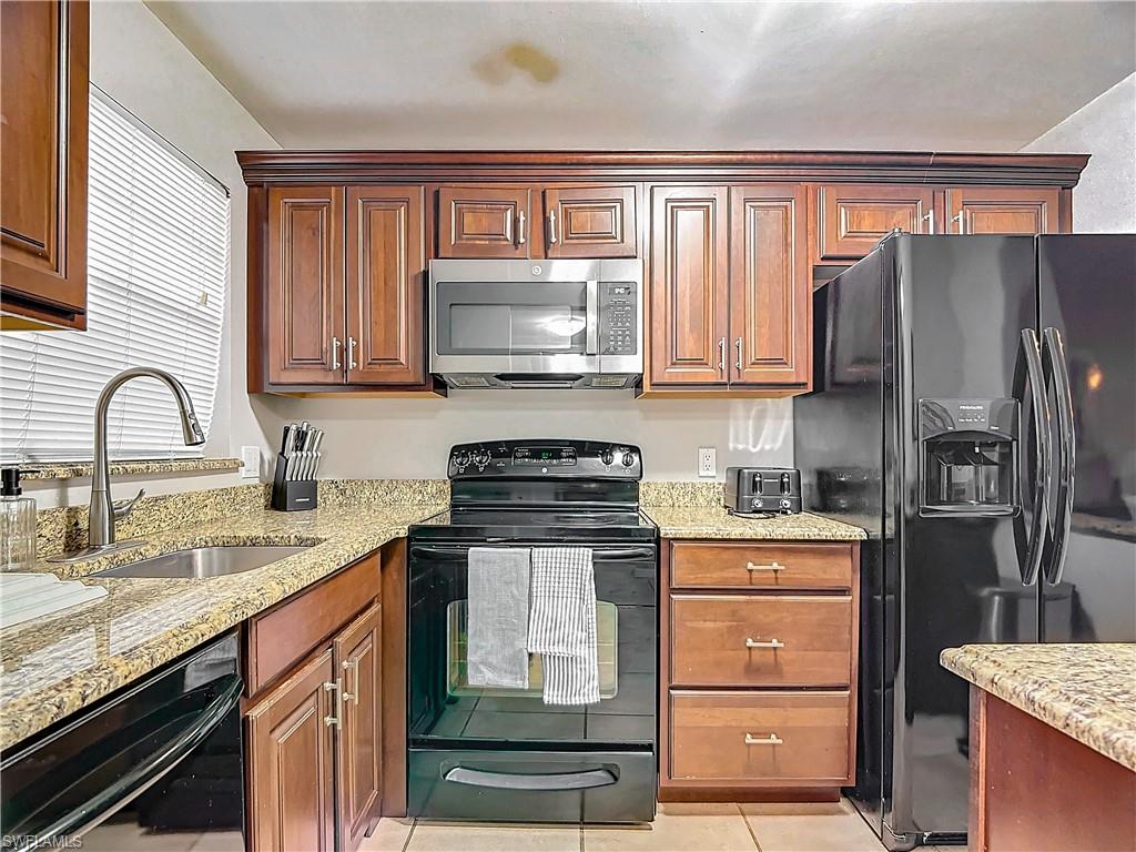 175 Turtle Lake Court, Unit 310 Naples, FL 34105 - Photo 5 of 34 Kitchen with light tile patterned flooring, light stone countertops, sink, and black appliances