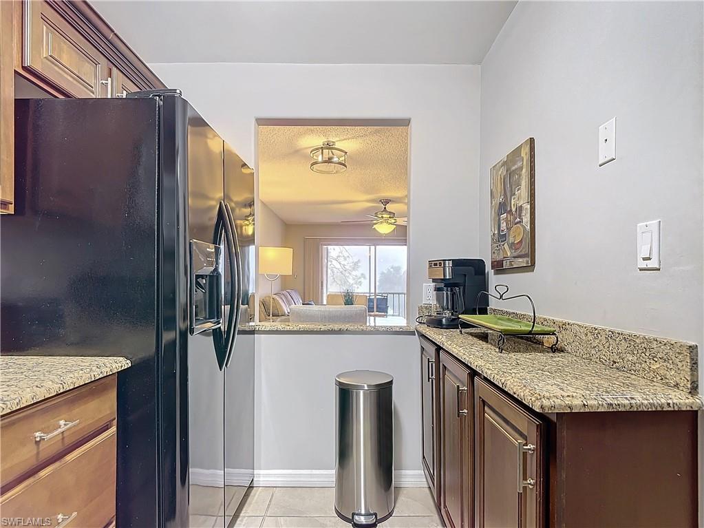 175 Turtle Lake Court, Unit 310 Naples, FL 34105 - Photo 7 of 34 Kitchen with light tile patterned floors, black refrigerator with ice dispenser, light stone countertops, and ceiling fan