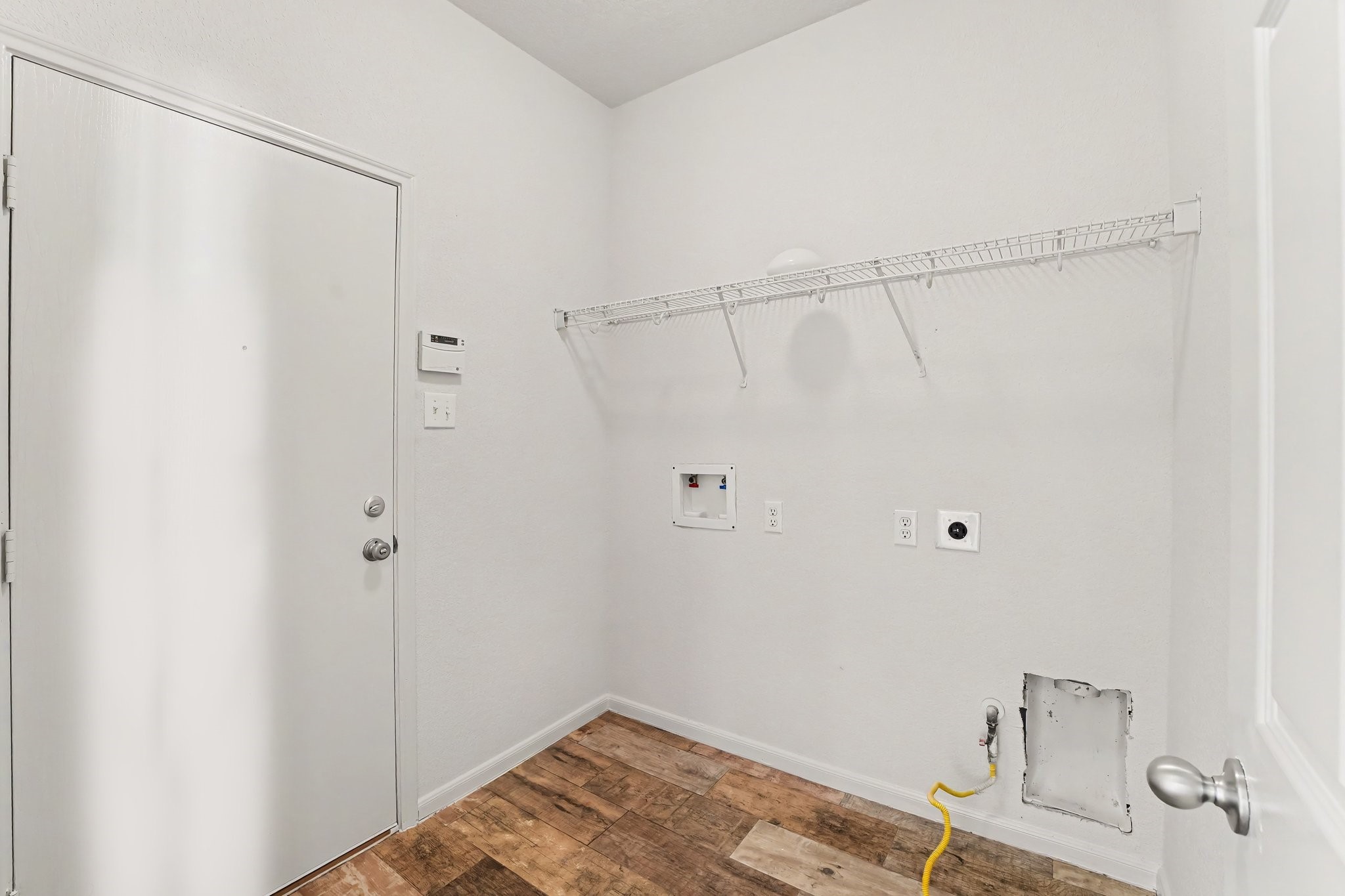 21427 Blooming Rock Lane Spring, TX 77379 - Photo 29 of 32 This photo shows a clean, white laundry room with a door, wire shelving, and hookups for a washer and dryer. The room features wood-look flooring and a simple, functional layout.