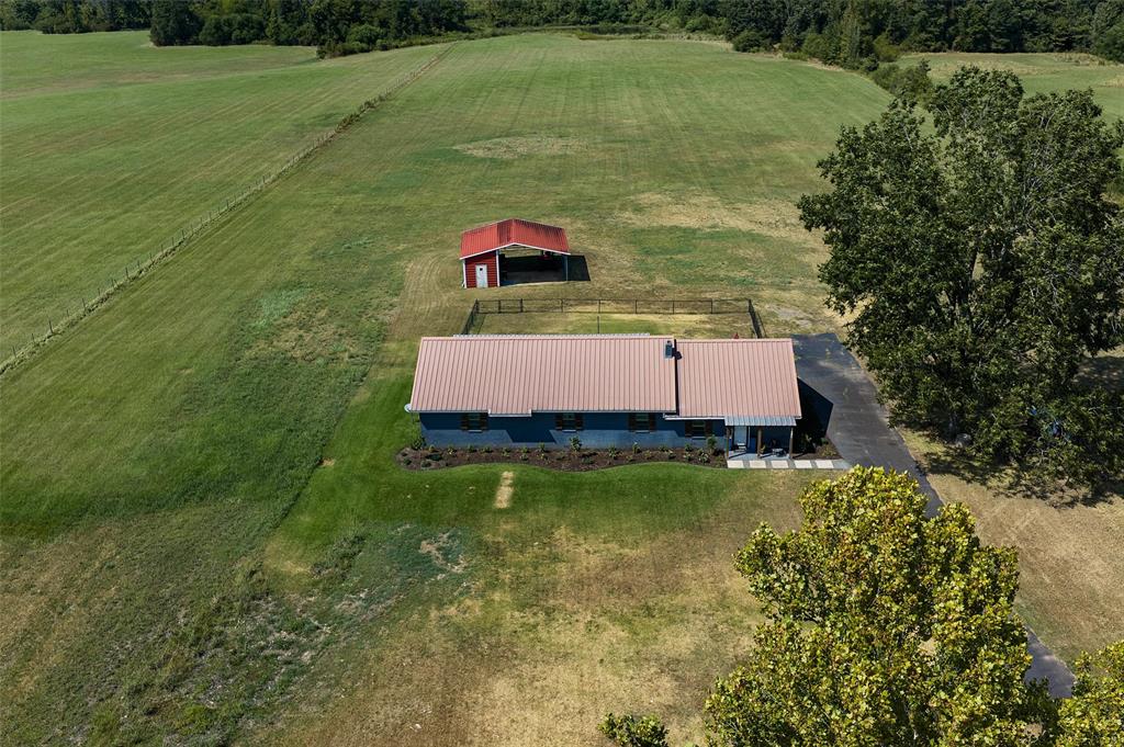 1131 Speights Road Keatchie, LA 71046 - Photo 2 of 33 Metal roof, dark blue exterior siding, paved driveway, detached red outbuilding, and extensive green fields
