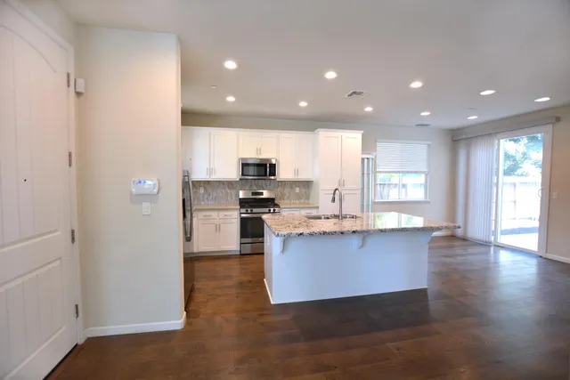 a kitchen with stainless steel appliances granite countertop a refrigerator a sink dishwasher a stove and white cabinets with wooden floor