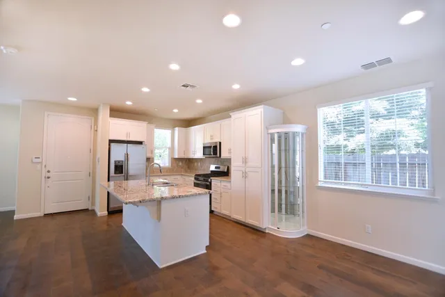 a open kitchen with stainless steel appliances granite countertop a refrigerator oven a sink and a large island with wooden floor