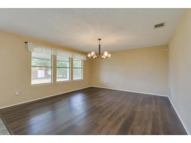 an empty room with wooden floor chandelier and windows