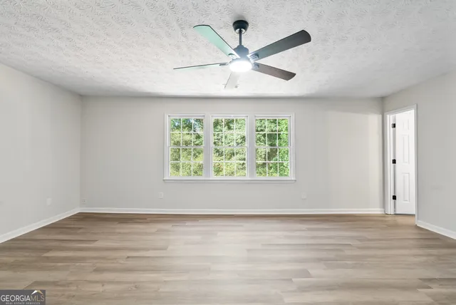 an empty room with wooden floor fan and windows