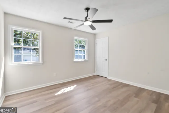 an empty room with wooden floor chandelier fan and windows