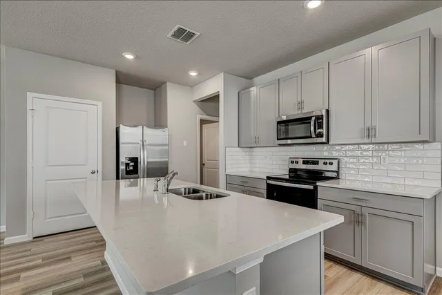 a kitchen with stainless steel appliances a stove top oven a sink a refrigerator white cabinets and wooden floor