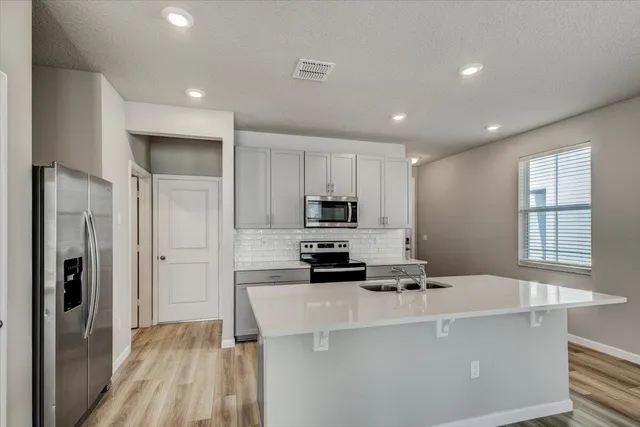 a kitchen with stainless steel appliances a stove a refrigerator a sink a microwave oven with white cabinets and wooden floor