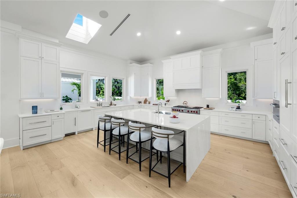 3136 Ravenna Avenue Naples, FL 34120 - Photo 21 of 50 Kitchen with a breakfast bar, an island with sink, light stone countertops, light wood-type flooring, and white cabinetry