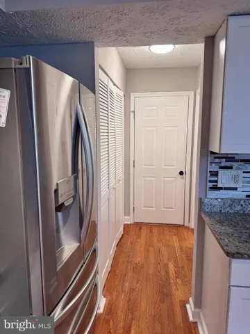 a view of a refrigerator in kitchen and an empty room with wooden floor