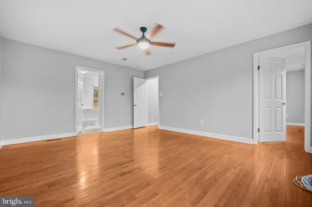 a view of an empty room with wooden floor and a ceiling fan